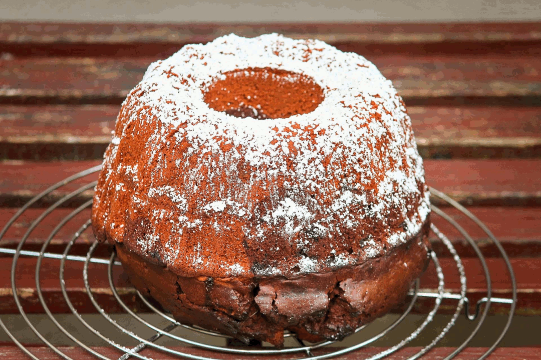 Bild eines Gugelhupfs. Ein kreisförmiger, brauner Kuchen mit weißem Staubzucker.